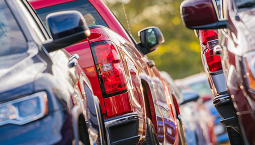 Close-up view of several parked cars in various colors, including red and blue, in a lot.