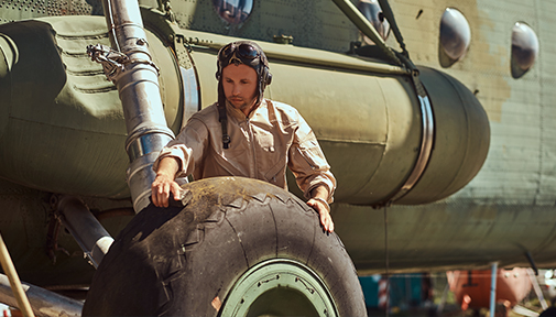 Military personnel inspecting the landing gear of a military aircraft.